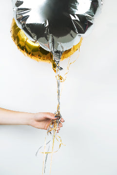 Hand holding a silver and gold foil balloon against a white background